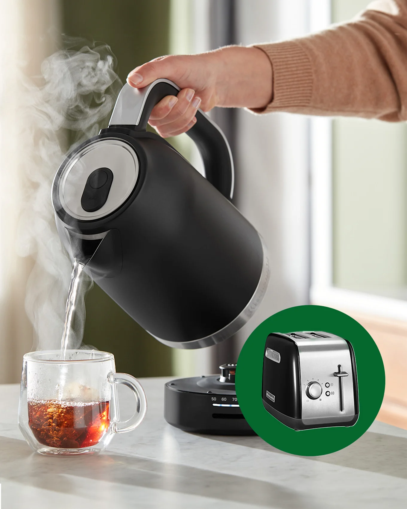 En hand häller ångande hett vatten från en svart vattenkokare i en tekopp av glas. En svart och stål brödrost visas i en infälld bild.