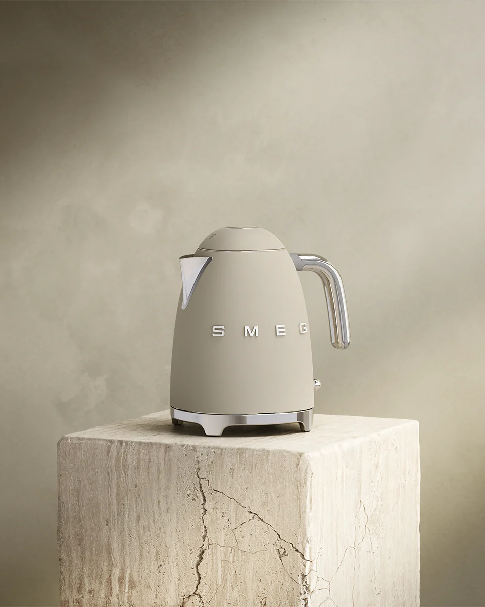 Beige Smeg vattenkokare med kromdetaljer på ett texturerat stenblock.