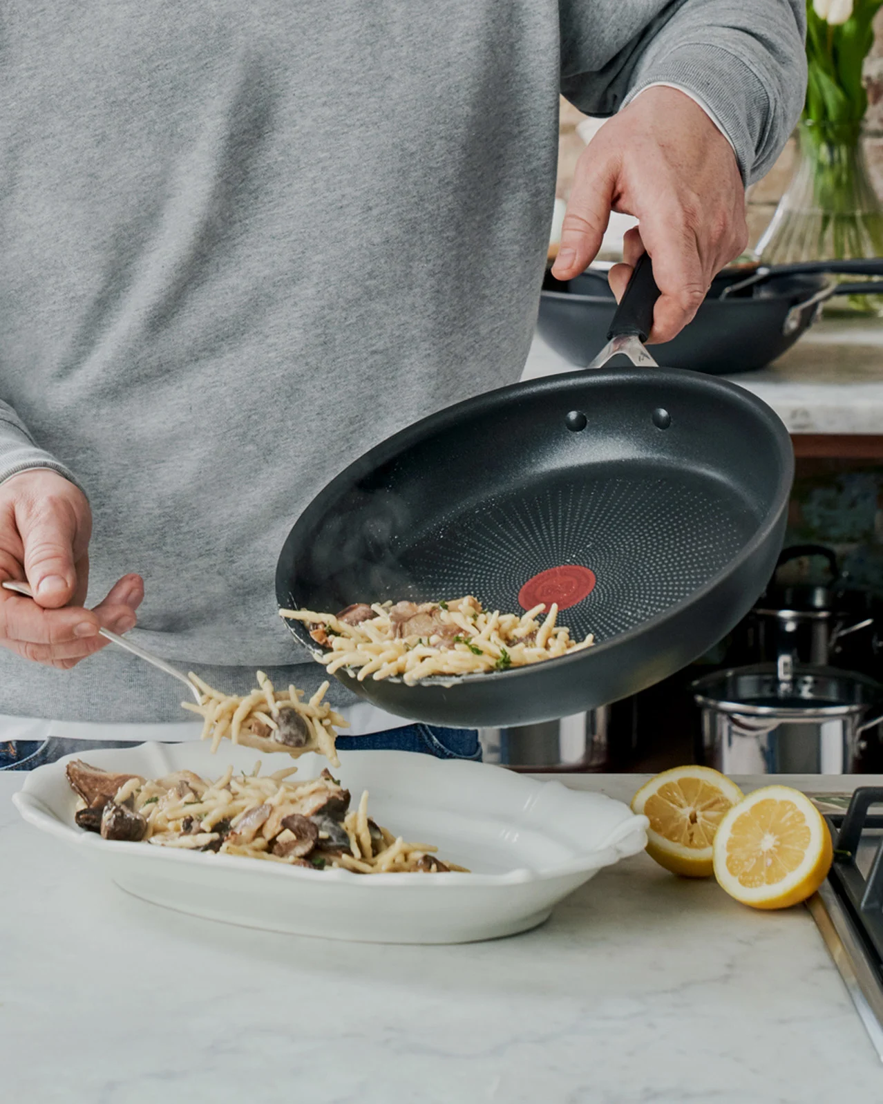 Person som serverar pasta med svamp från en stekpanna till en serveringsskål.